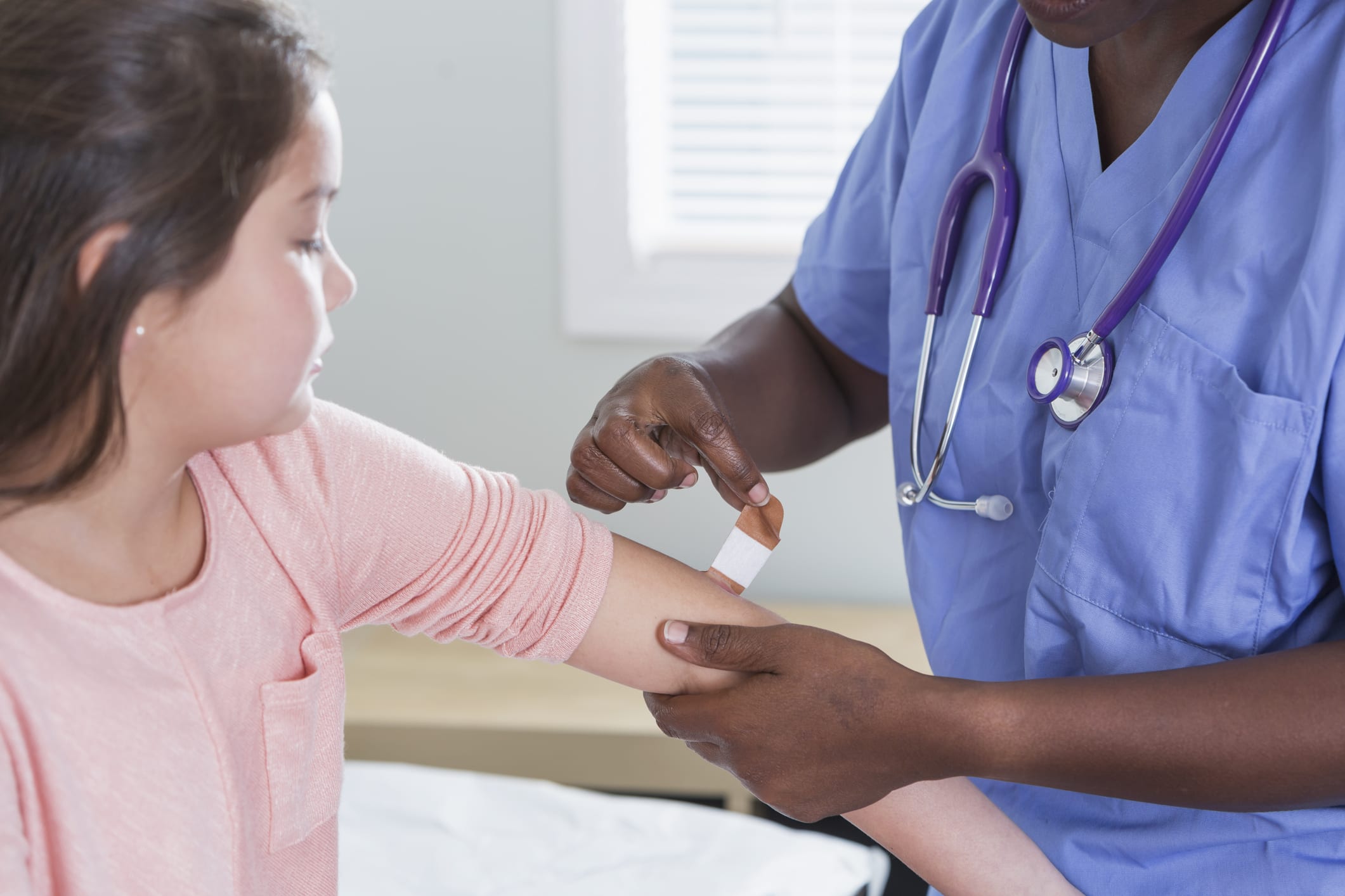 Cropped view of a female doctor or nurse smiling at the camera as she puts an adhesive bandage on the arm of her young patient, a 9 year old girl.