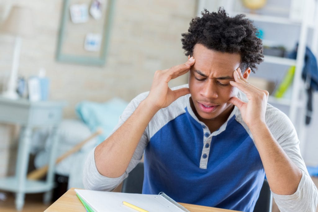 Frustrated teenage boy has is head in is hands in frustration while working on homework assignment.